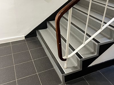 Grey checked floor with grey stairs and a white and brown handrail