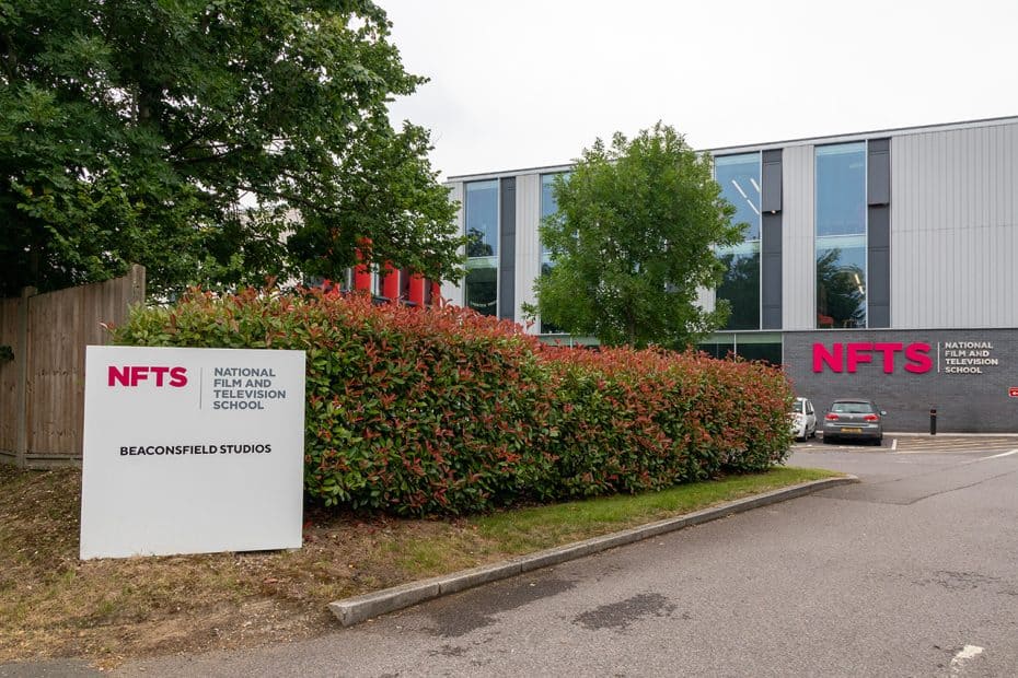 Entrance to the National Film and Television School. White sign with logo and name on left hand side. Building in background with name and logo.