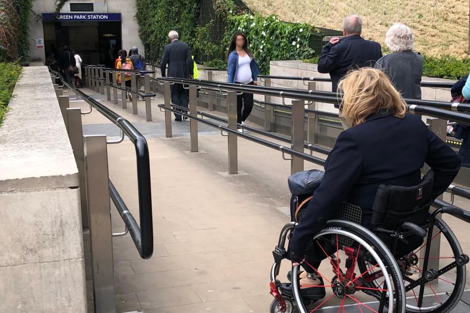 Aquí tienes un texto alternativo (alt text) muy breve y claro, descriptivo y accesible: Alt text: A wheelchair user approaches the step-free ramp entrance of Green Park Underground Station in London.
