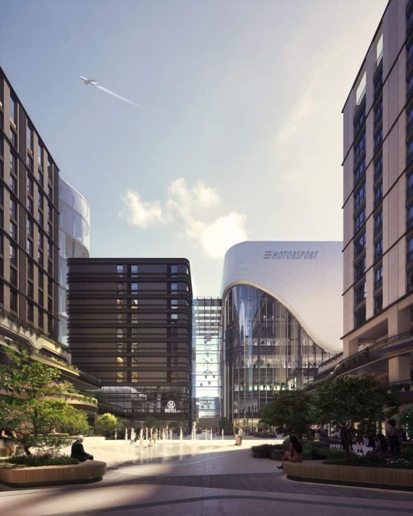Artist's impression of London Motorsports campus. There are tall buildings to the right and left with a landscaped area to the front with a water fountain. There is a tall building in the middle. The bottom half is glass while the top is solid white with the word Motorsport. The building on the left has the word hotel.